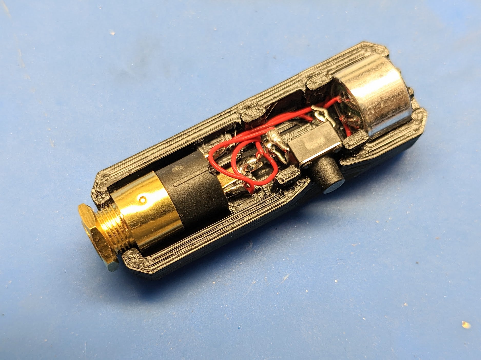 The bottom half of a black printed case with the 3.5mm jack, push switch and mic element pressed into place and the red wires tucked into the centre channel