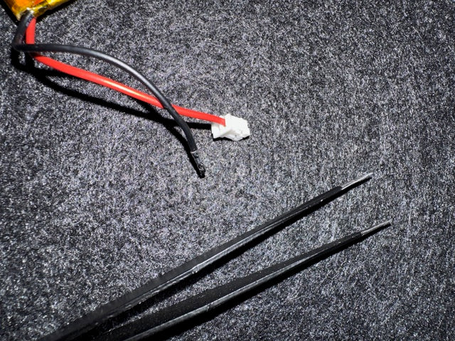 One wire removed from the battery plug The battery’s JST plug with the black wire pulled out of its slot, next to a pair of tweezers