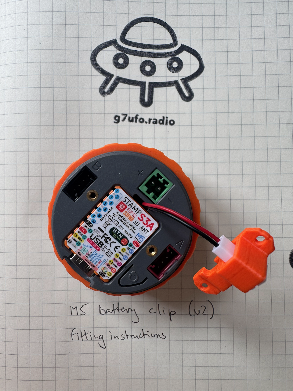The STAMP S3A board refitted with the battery cable fed out The STAMP S3A board refitted in the M5 Dial, with the battery clip’s red and black cable running out of the groove at the top of the board to the orange battery adapter
