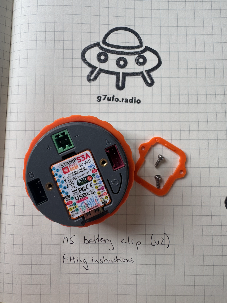 The back panel clip and screws removed The back of the M5 Dial with the orange back panel clip and its two screws removed, exposing the STAMP S3A board