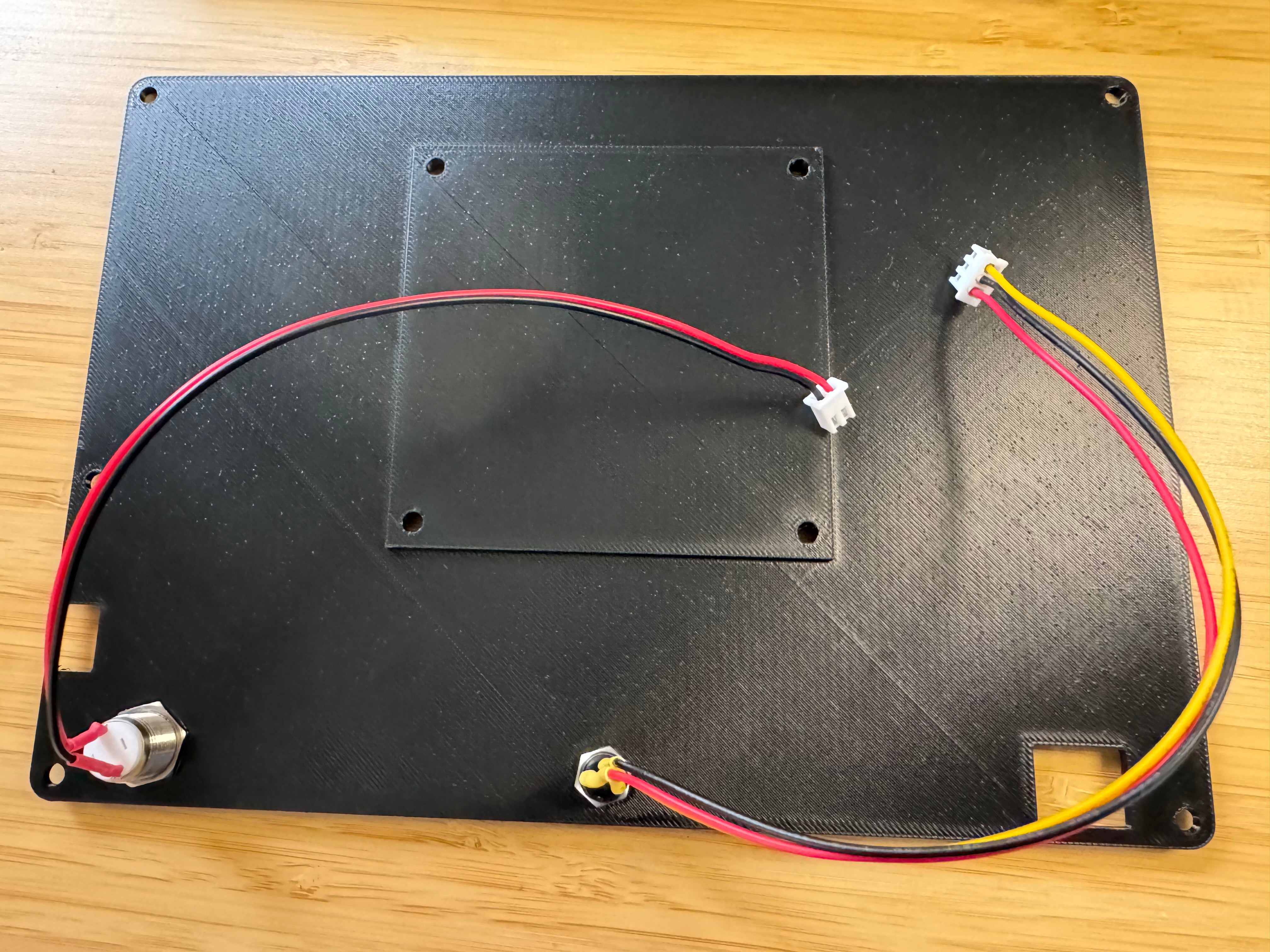 The inside of the black printed back panel with the power button and a 3.5mm socket fitted, each wired to a JST connector