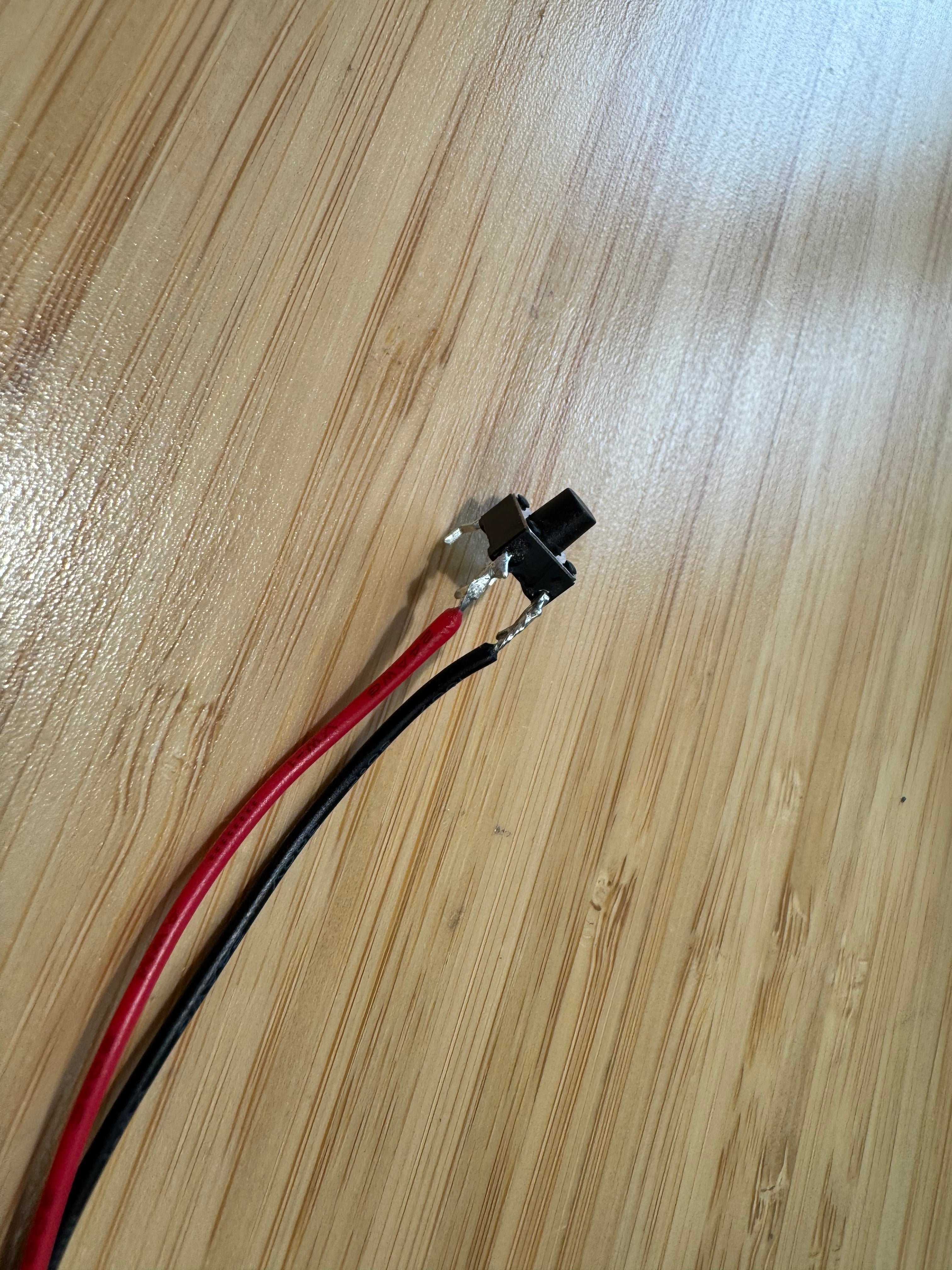 A 6mm tactile push switch with a red and a black wire soldered to two of its legs